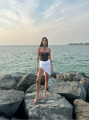 Caletta White 100% Cotton Pareo (beach wrap) styled as a short skirt on a model by the sea. Ideal for resort wear.